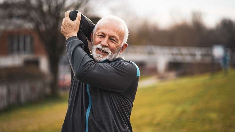 Older man in sweatsuit stretching outdoors