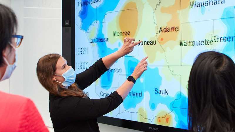 Three researchers using an interactive geospatial cancer map on a large screen display