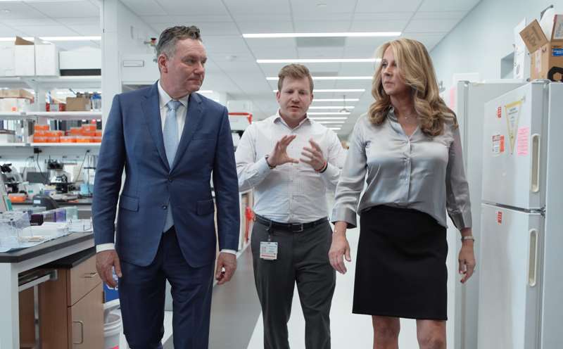 Tim and Barbara Michels walk through cancer laboratory with researcher Matthew Kudek